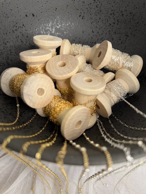 Wooden spools of gold and silver chain in a dark bowl