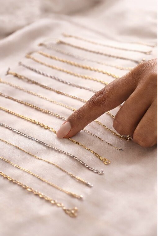 Gold and silver chains laid out in rows as a finger points to one