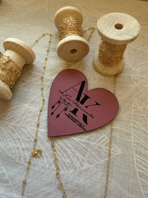 A heart-shaped A.Kai logo tag with spools of gold chain